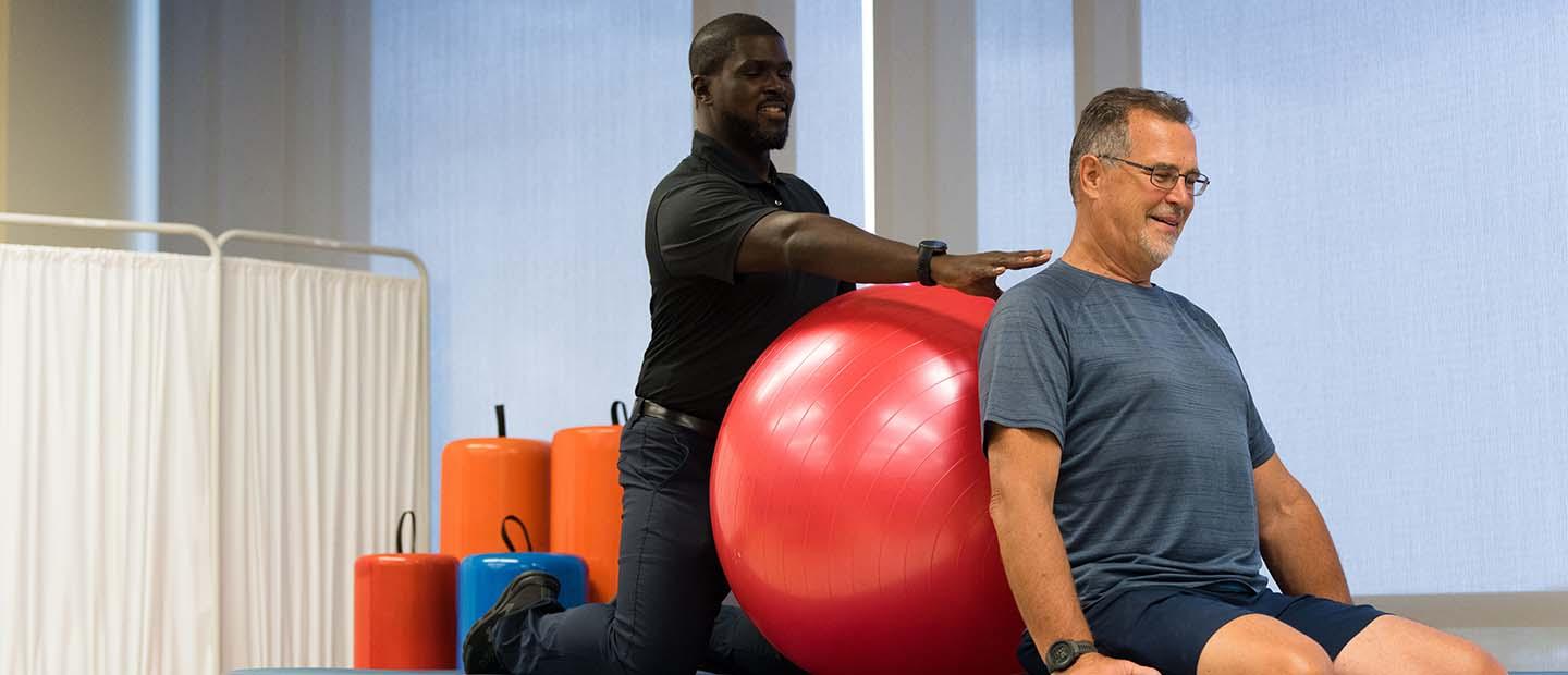 一名男性理疗师在健身房的桌子上帮助一名男子拿健身球.